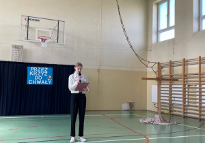 Uczennica podczas przedstawienia z okazji Wielkanocy na sali gimnastycznej odczytuje tekst.