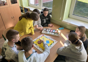 Uczniowie siedzą w ławkach i grają w grę planszową Eurobiznes