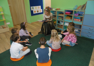Dzieci z oddziału przedszkolnego słuchają bajki czytanej przez Panią z Gminnej Biblioteki Publicznej w Rzgowie