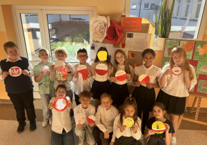 Uczniowie prezentują wykonane proporczyki na tle wystawy dotyczącej Bohaterek Powstania Warszawskiego