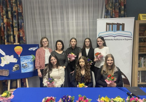 Uczestniczy i organizatorzy wieczorku poetyckiego pozują do zdjęcia z kwiatami