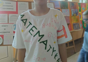 Uczennica przedstawia włesnoręcznie zrobioną matematyczną koszlkę