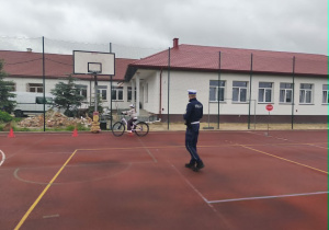 Policjant obserwuje jak porusza się uczennica na rowerze